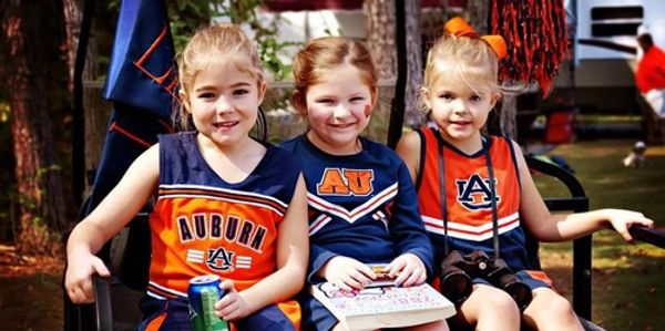 Three young girls in Auburn cheerleading uniforms sitting outdoors.