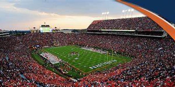 A packed football stadium during a game at sunset.