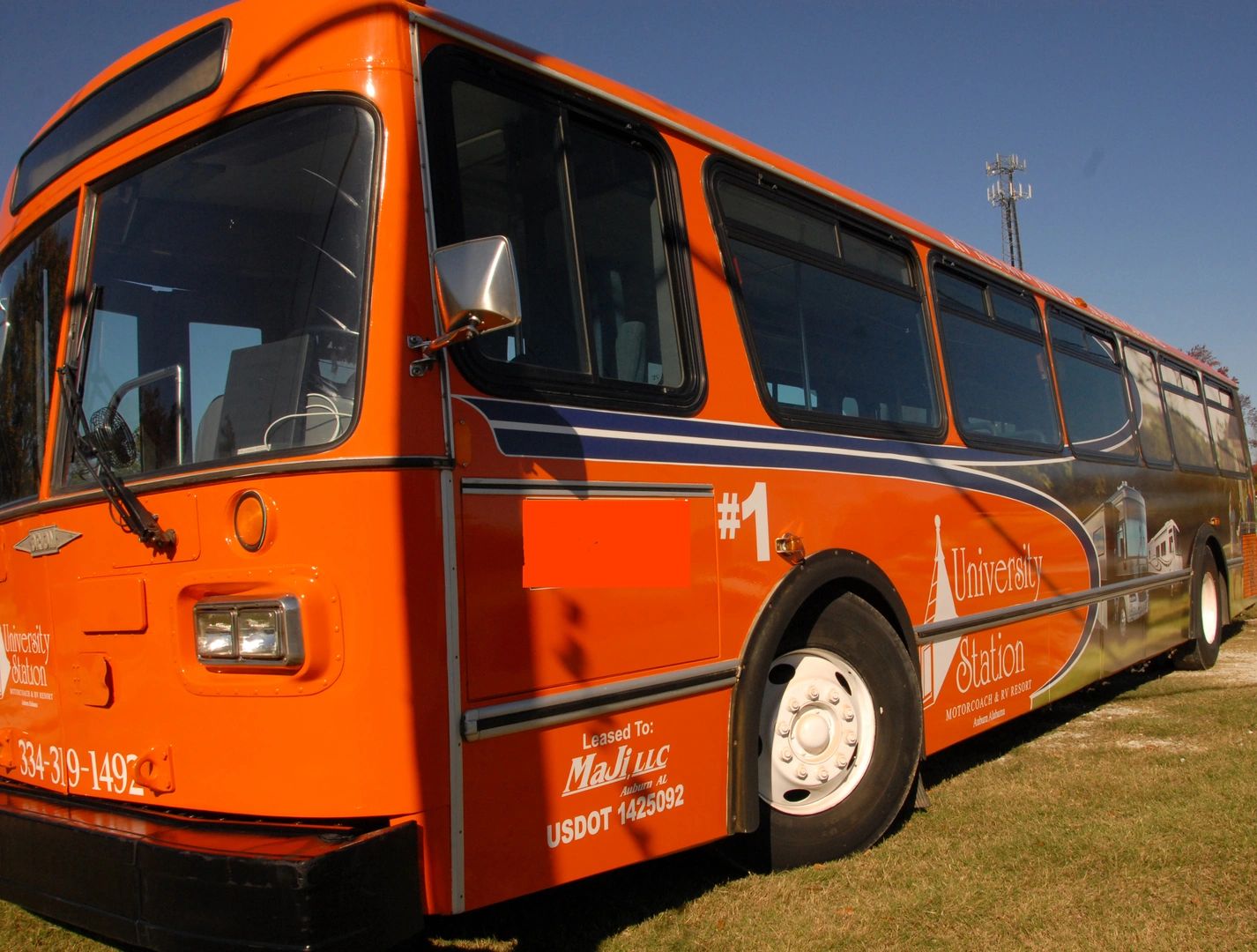 Orange university shuttle bus parked on grass under a clear sky.