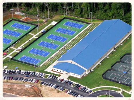 Aerial view of multiple pickleball courts with a large blue-roofed building nearby.